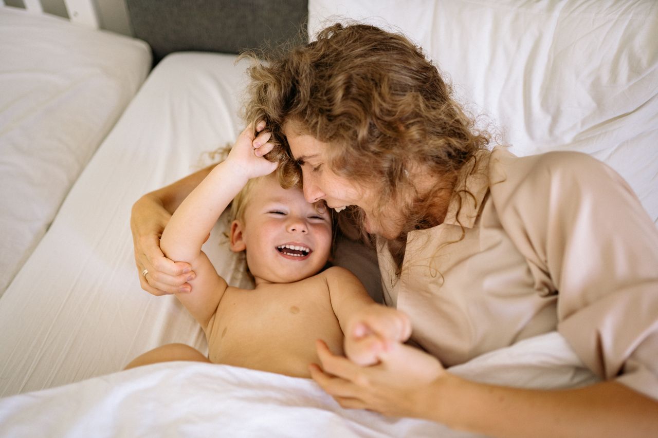 The Art of Drawing Readers In: Your attractive post title goes here Joyful mother and child sharing a playful moment in bed. Heartwarming family scene.